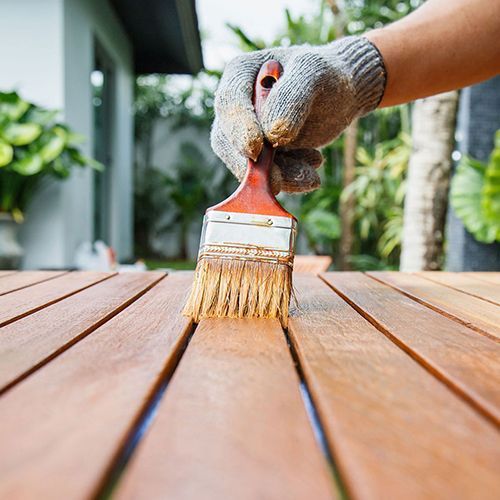 A person is applying a wood stain onto a wooden surface using a brush
