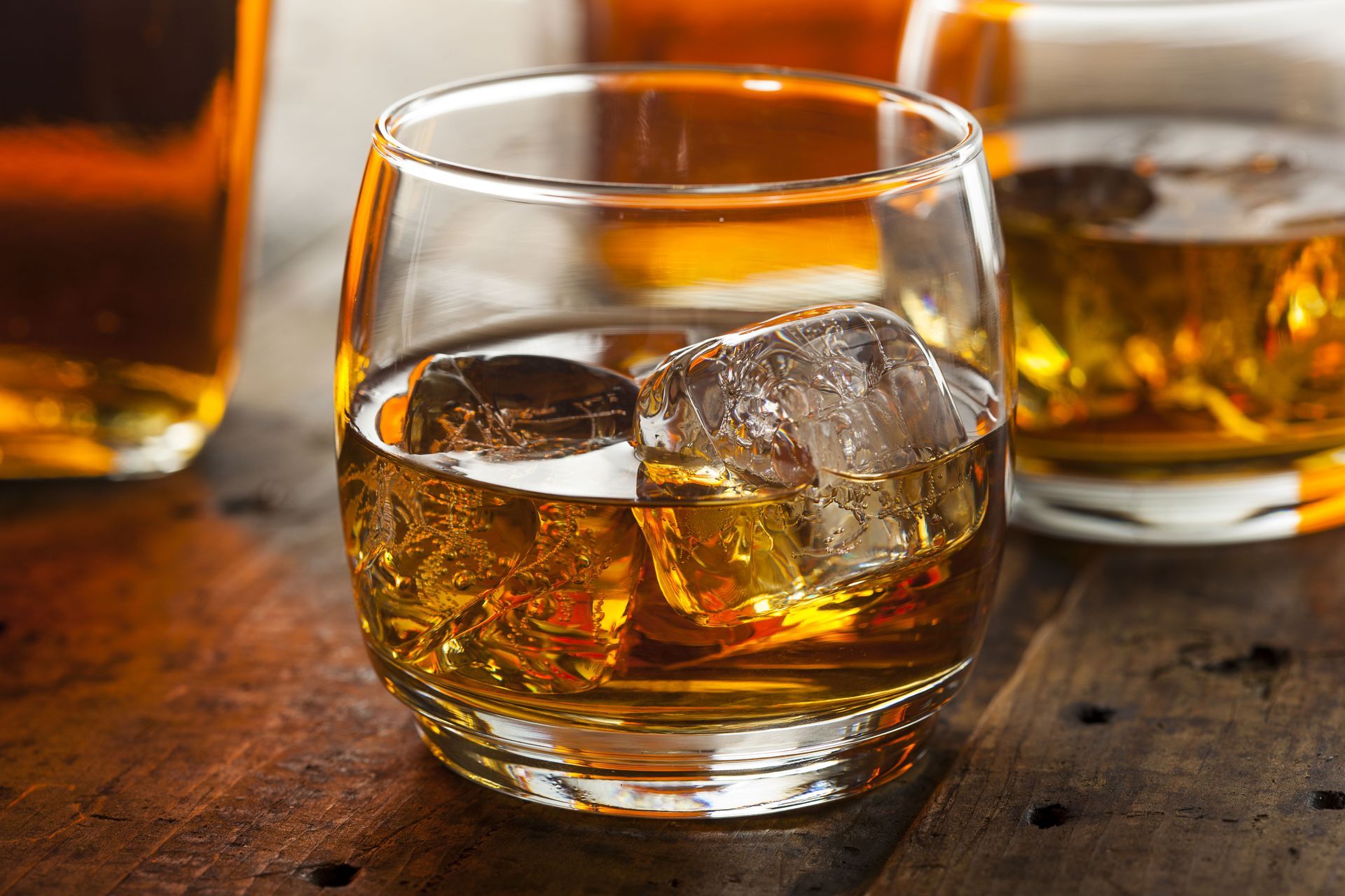 Whiskey on the rocks in a glass tumbler, with ice cubes, against a blurred background.