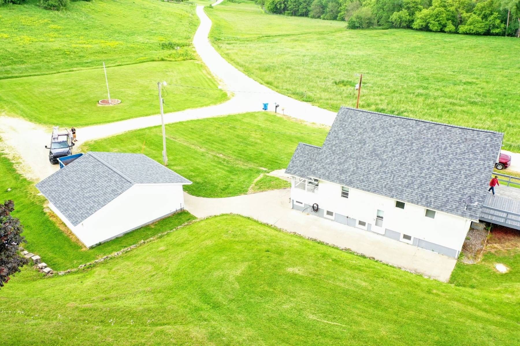 Aerial view of two white houses with gray roofs beside green fields and a winding path