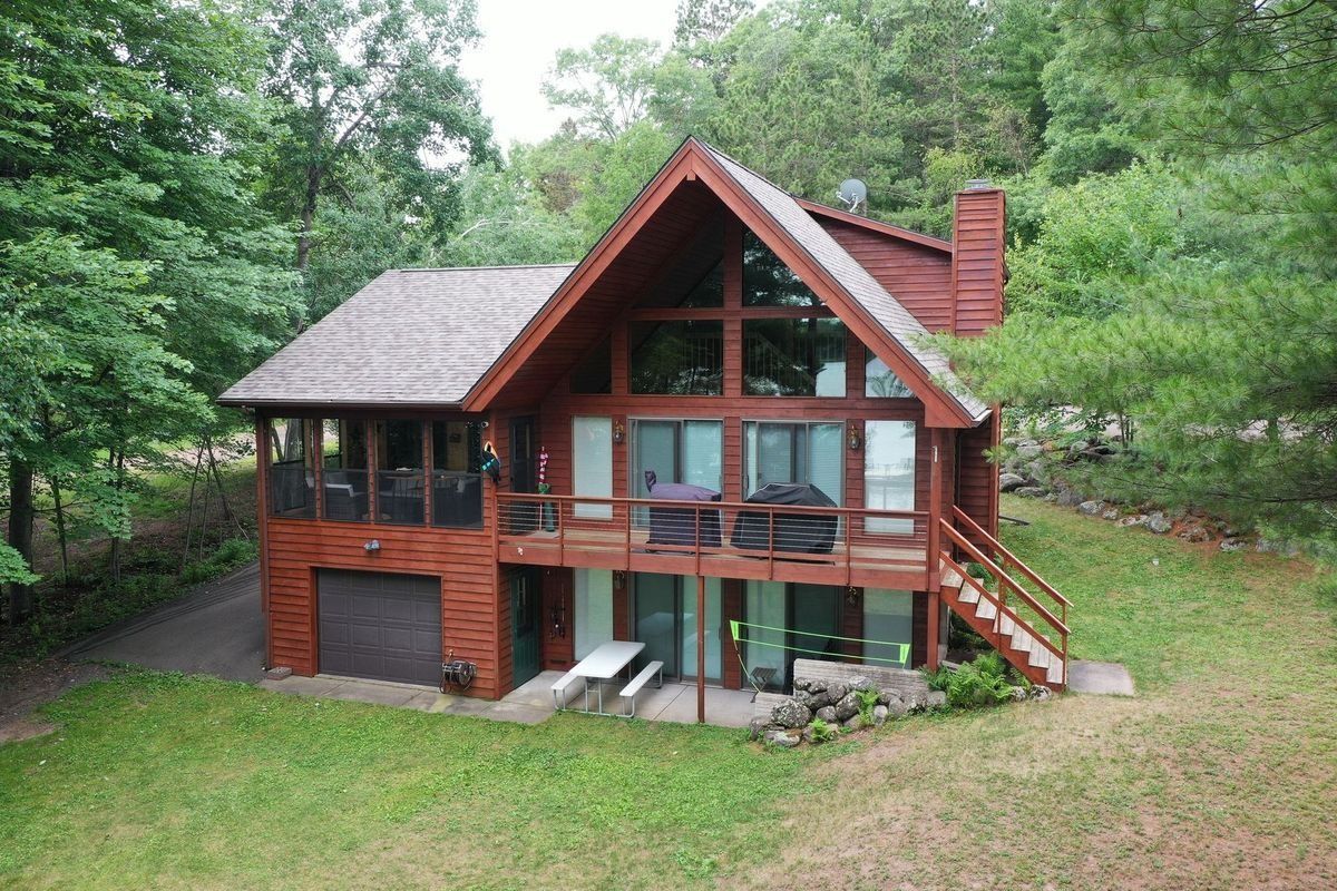 Wooden cabin with large windows and a deck, nestled in a green wooded hillside