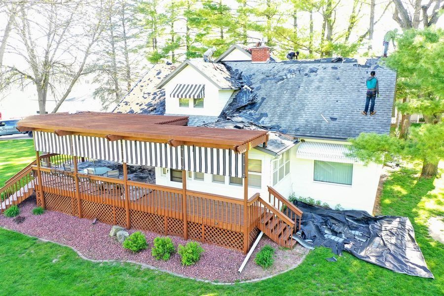 House with a wooden porch and pergola, gray roof, and a person standing on the roof in a green yard