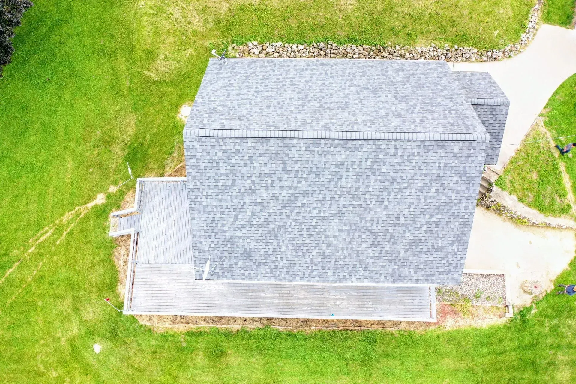 Aerial view of a gray-roofed house with a wooden deck surrounded by bright green grass.