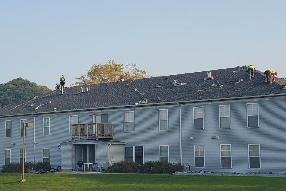 Gray apartment building with a dark roof and small balconies on a grassy lawn under a clear sky