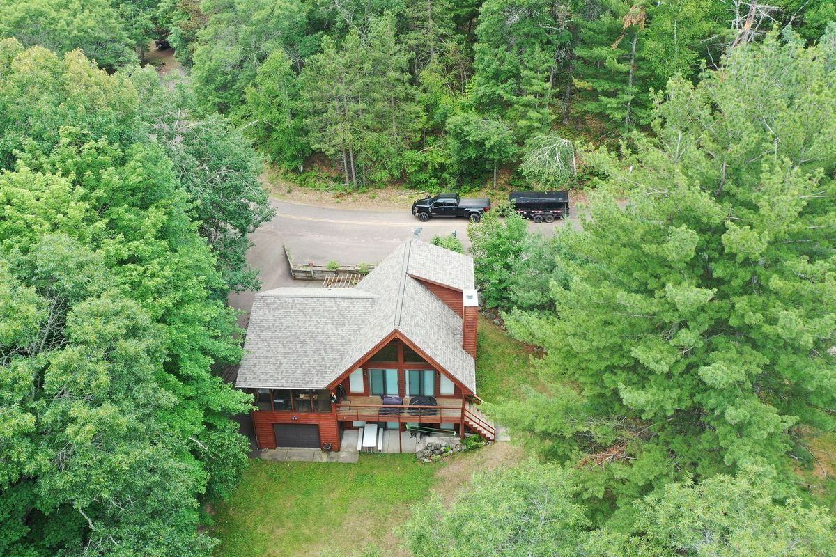 Aerial view of a cabin with a steep roof surrounded by dense green trees.