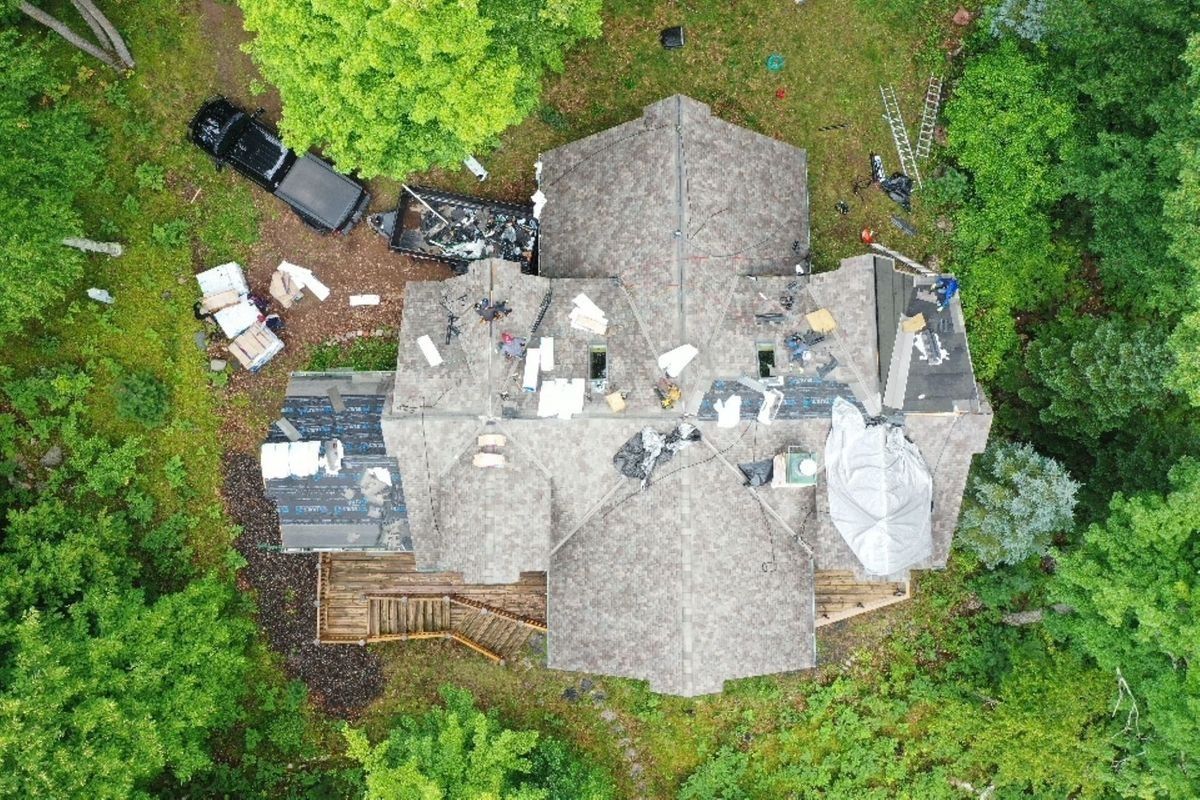 Aerial view of a house roof surrounded by trees, with scattered items and a truck beside it