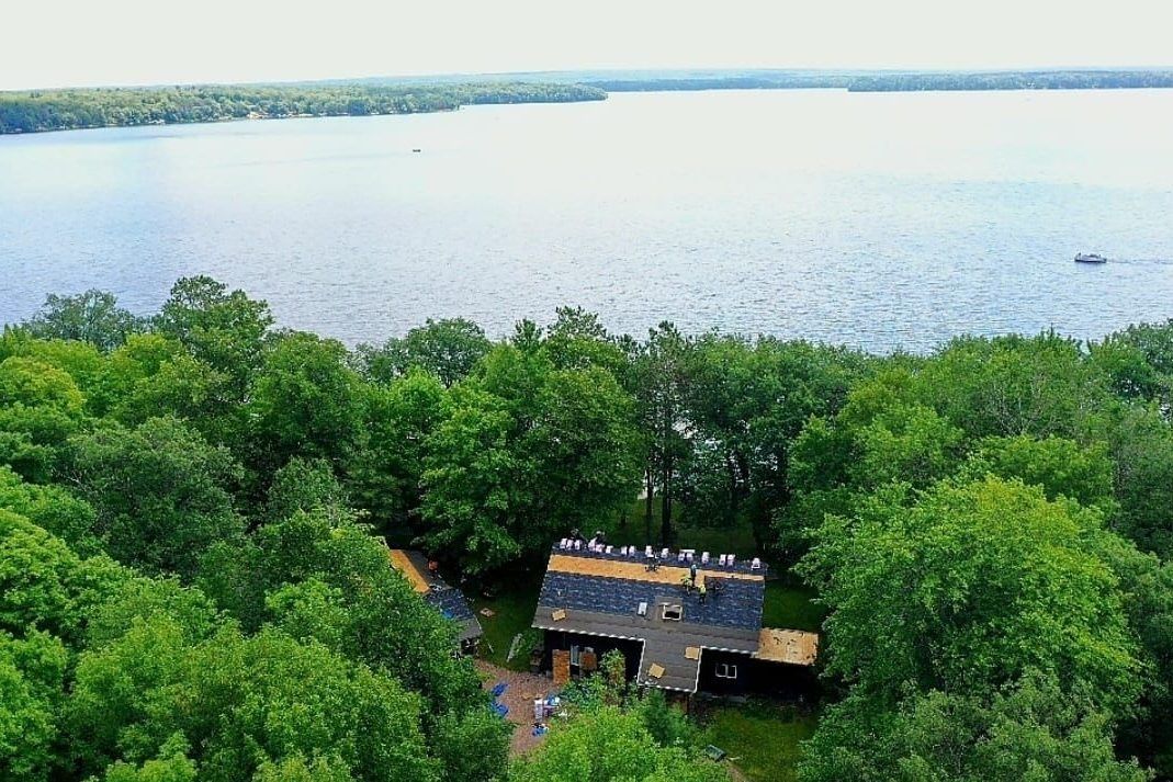 Aerial view of a small cabin amid green trees beside a large lake