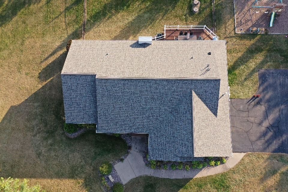 Aerial view of a gray-roofed house with a small backyard patio and surrounding grass yard.