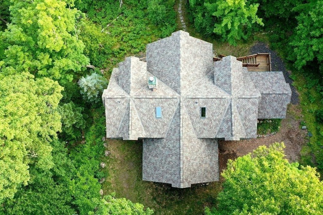 Top-down view of a gray-roofed house surrounded by dense green trees