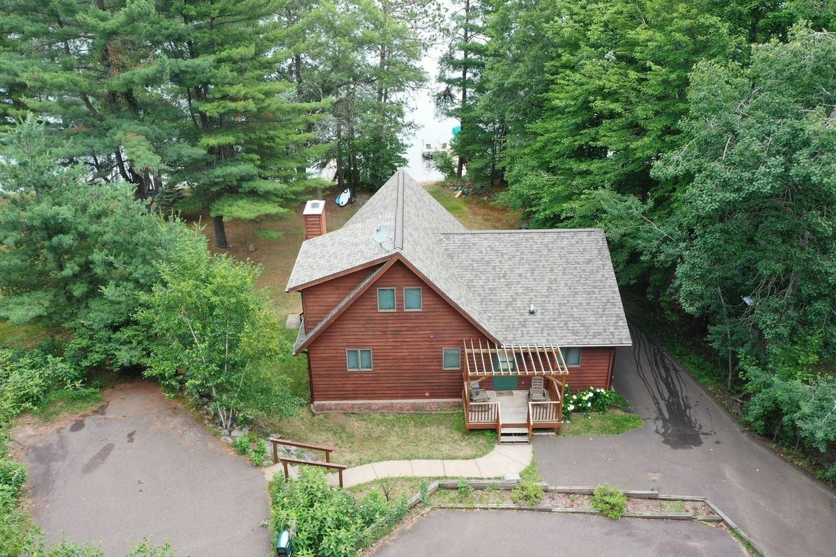 Aerial view of a rustic red cabin surrounded by lush green trees and a driveway.