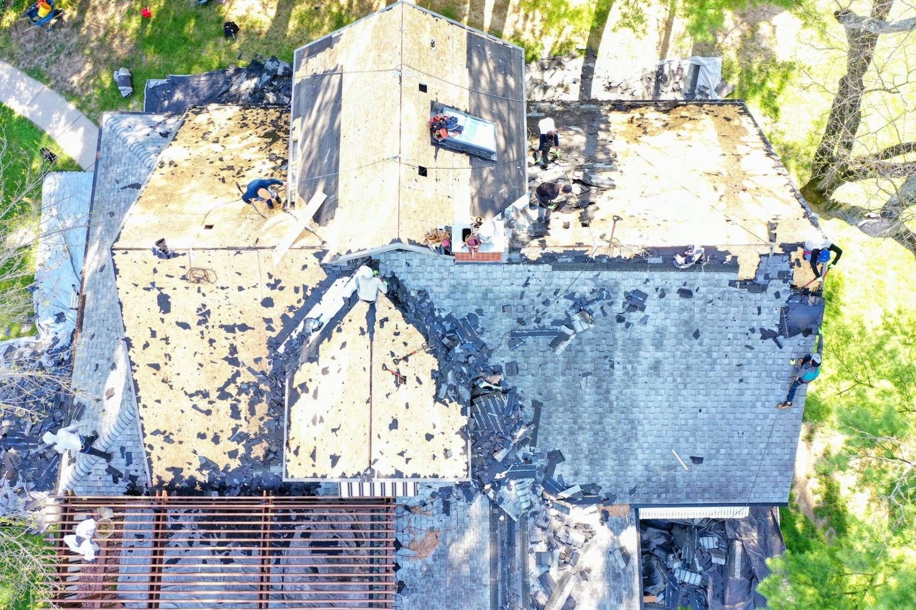 Aerial view of a weathered rooftop with two adjoining gray and beige sections, surrounded by trees.