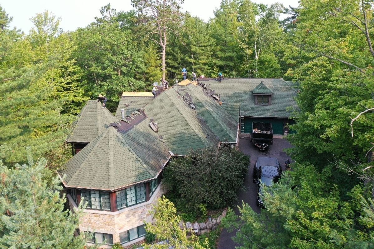 A large green-roofed house nestled among dense trees, viewed from above.