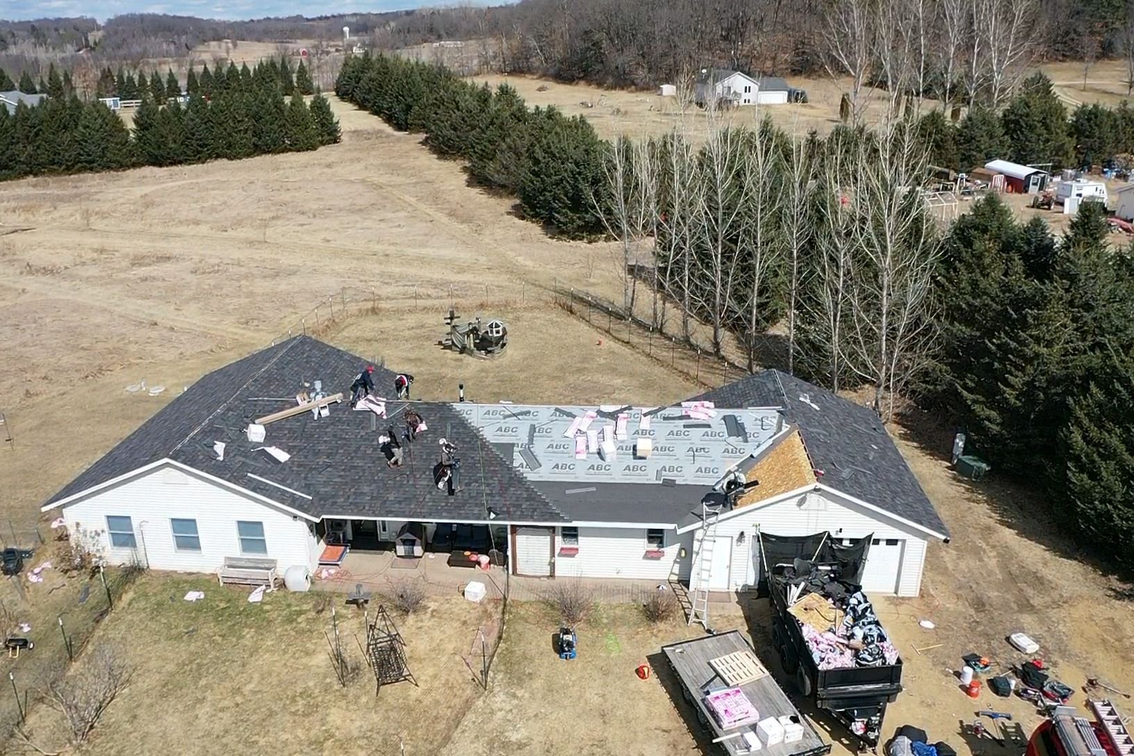Aerial view of a house with roof damage and debris in a rural field after a storm