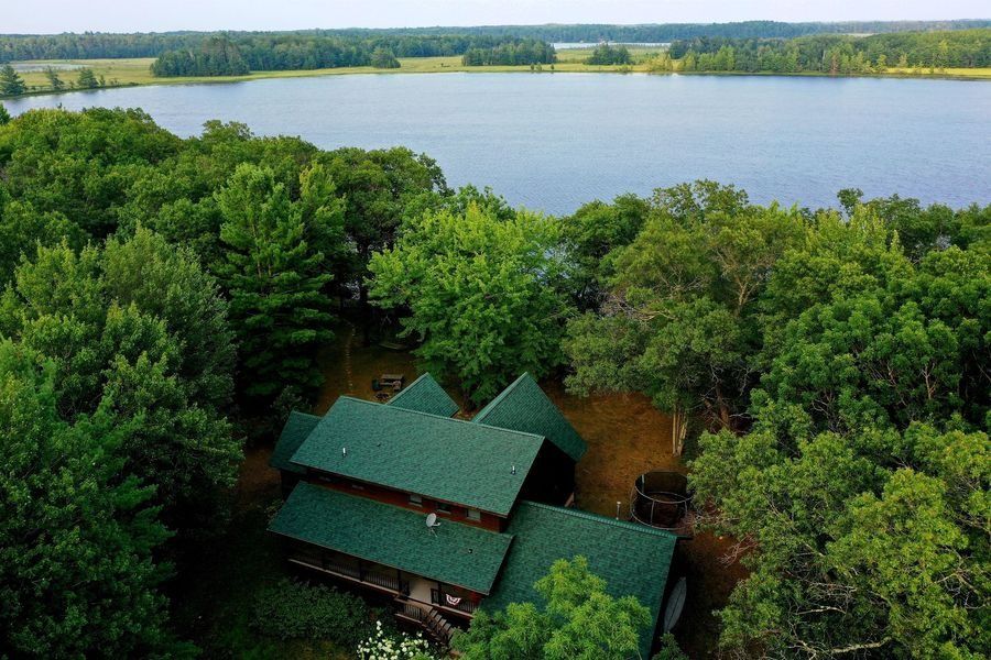 A green-roofed cabin nestled among trees beside a lake with a wide shoreline view.