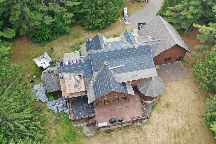 Aerial view of a damaged house with a partially collapsed roof, surrounded by trees and grass.