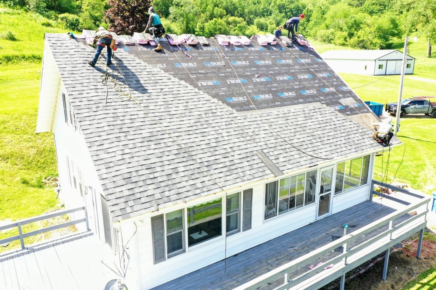 Workers installing shingles on a house roof with a dark underlayment exposed