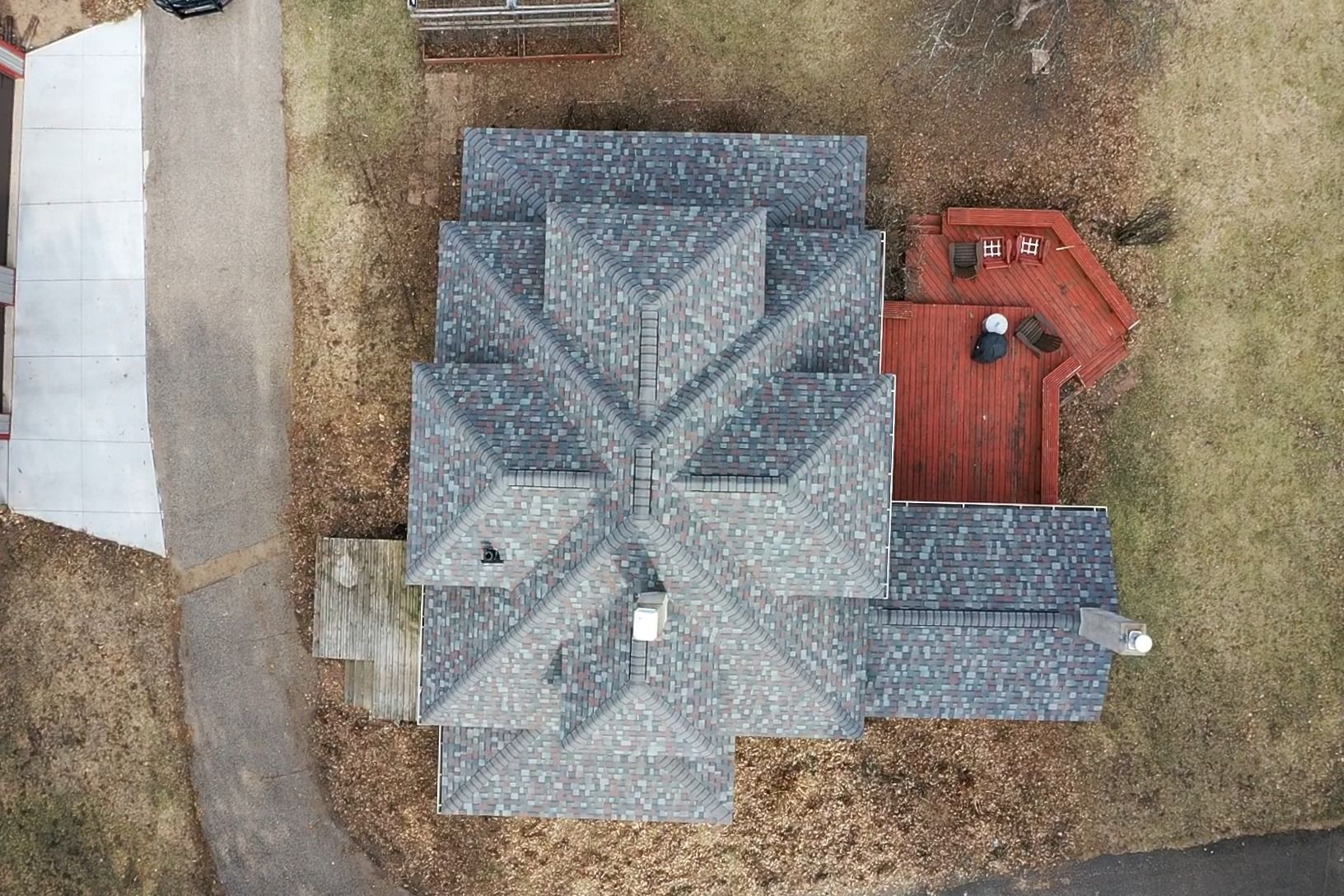 Aerial view of a gray-roofed house with a red deck and surrounding yard.