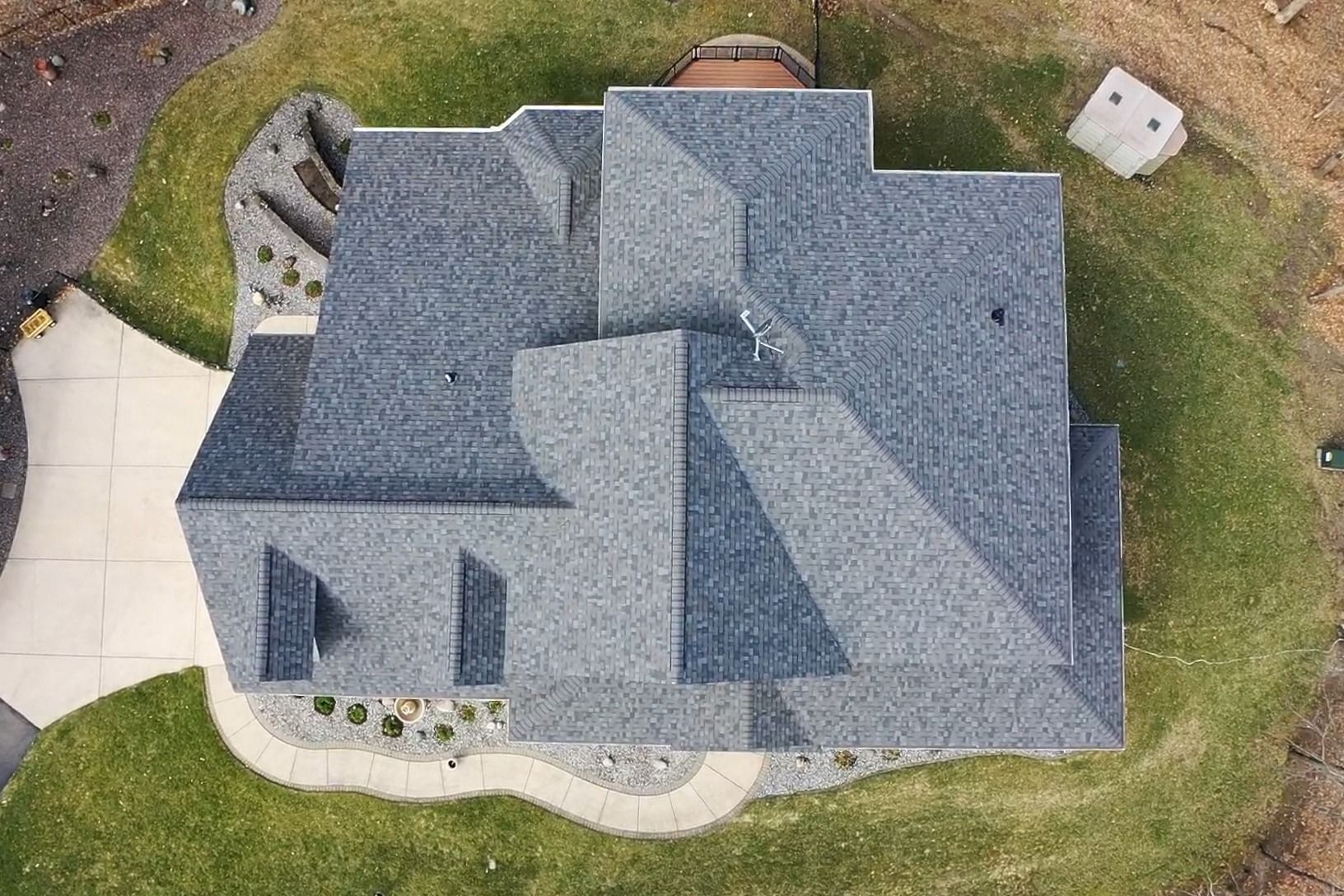Aerial view of a gray-roofed suburban house with lawn, driveway, and surrounding yard