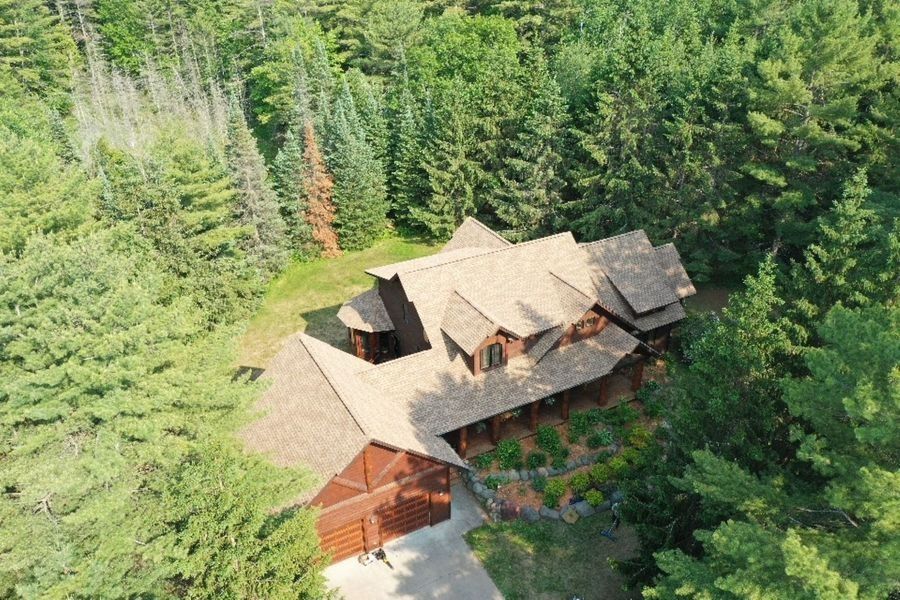 Aerial view of a large wooden cabin with a brown roof surrounded by dense green forest.