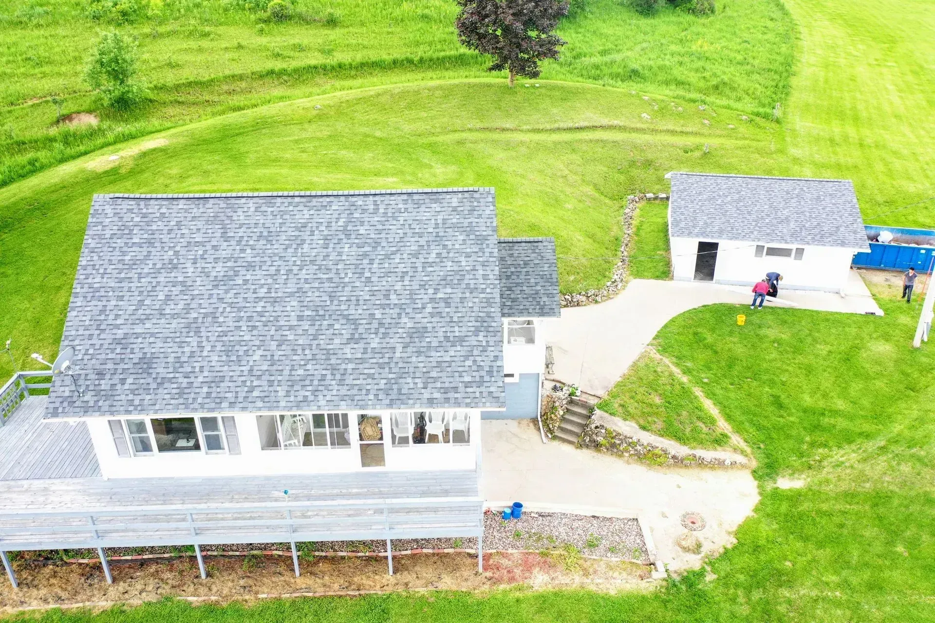 Aerial view of two gray-roofed buildings connected by a walkway, surrounded by bright green lawn.