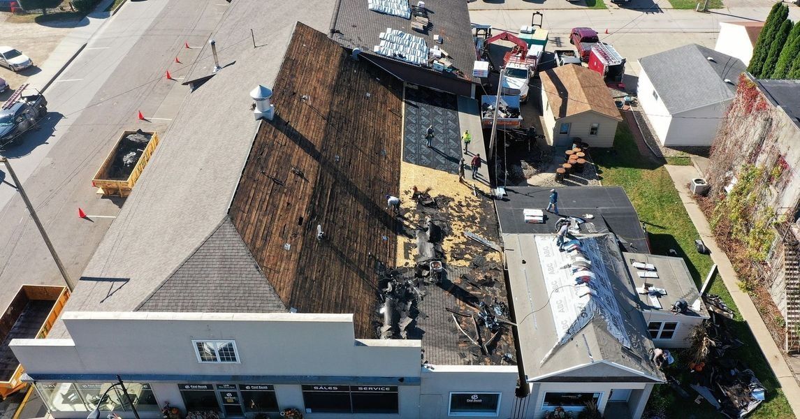 Aerial view of a fire-damaged building with a collapsed roof and debris beside neighboring structures.