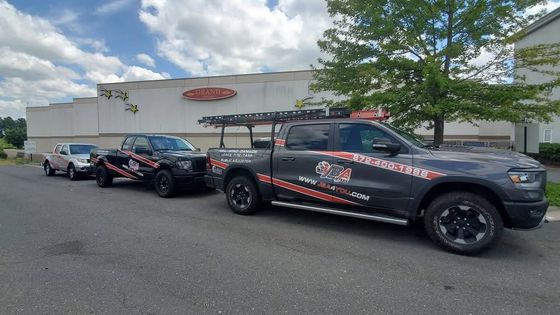Black pickup truck with trailer in a parking lot outside a white building on a cloudy day