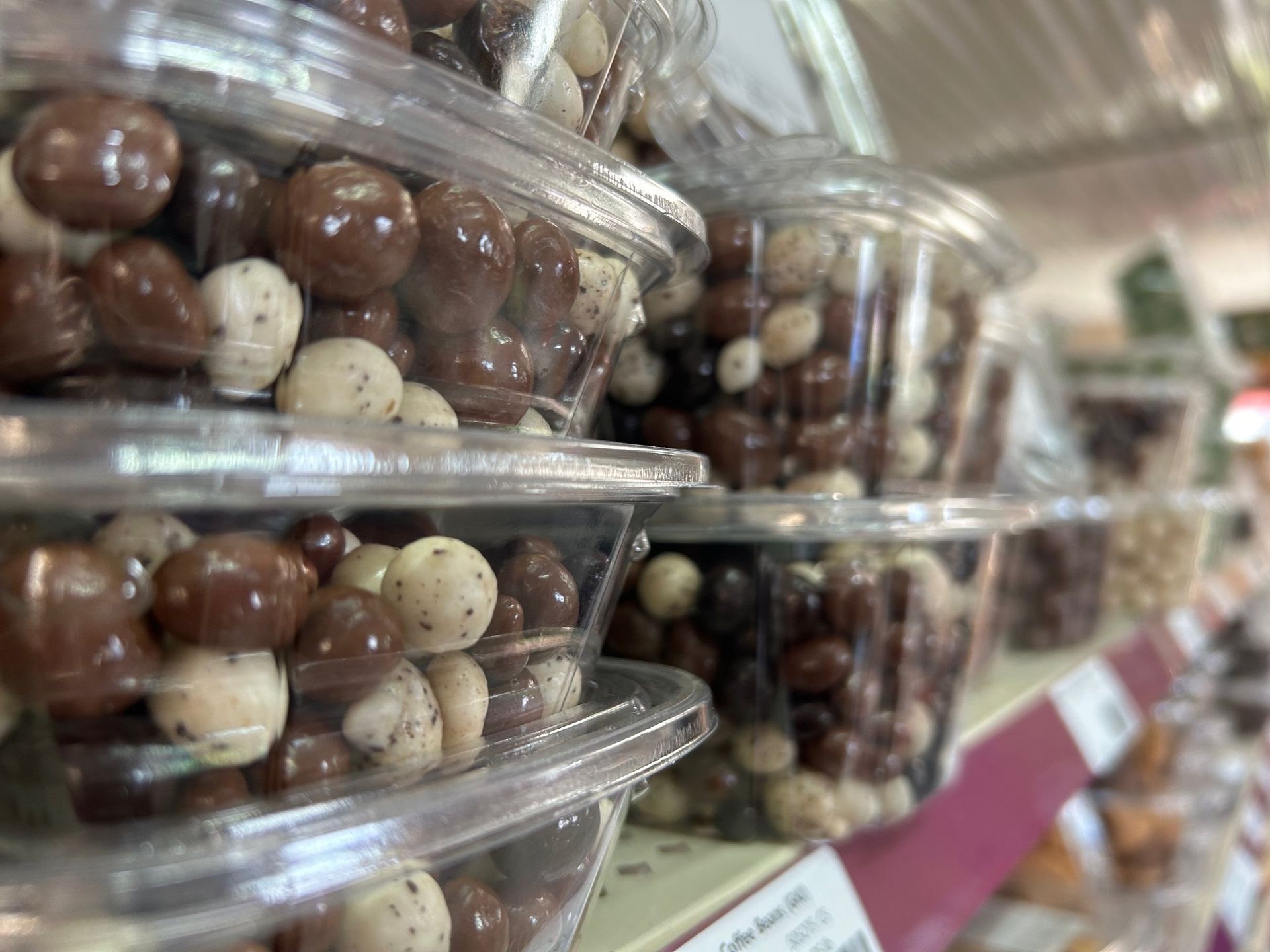 A shelf filled with plastic containers filled with chocolate covered nuts.