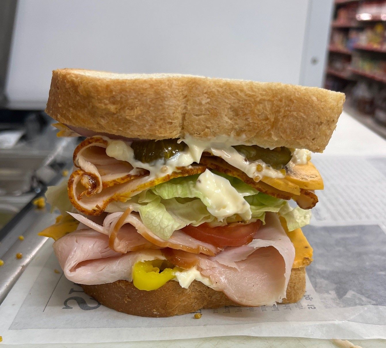 A sandwich with ham, lettuce, tomatoes and cheese is sitting on a table.