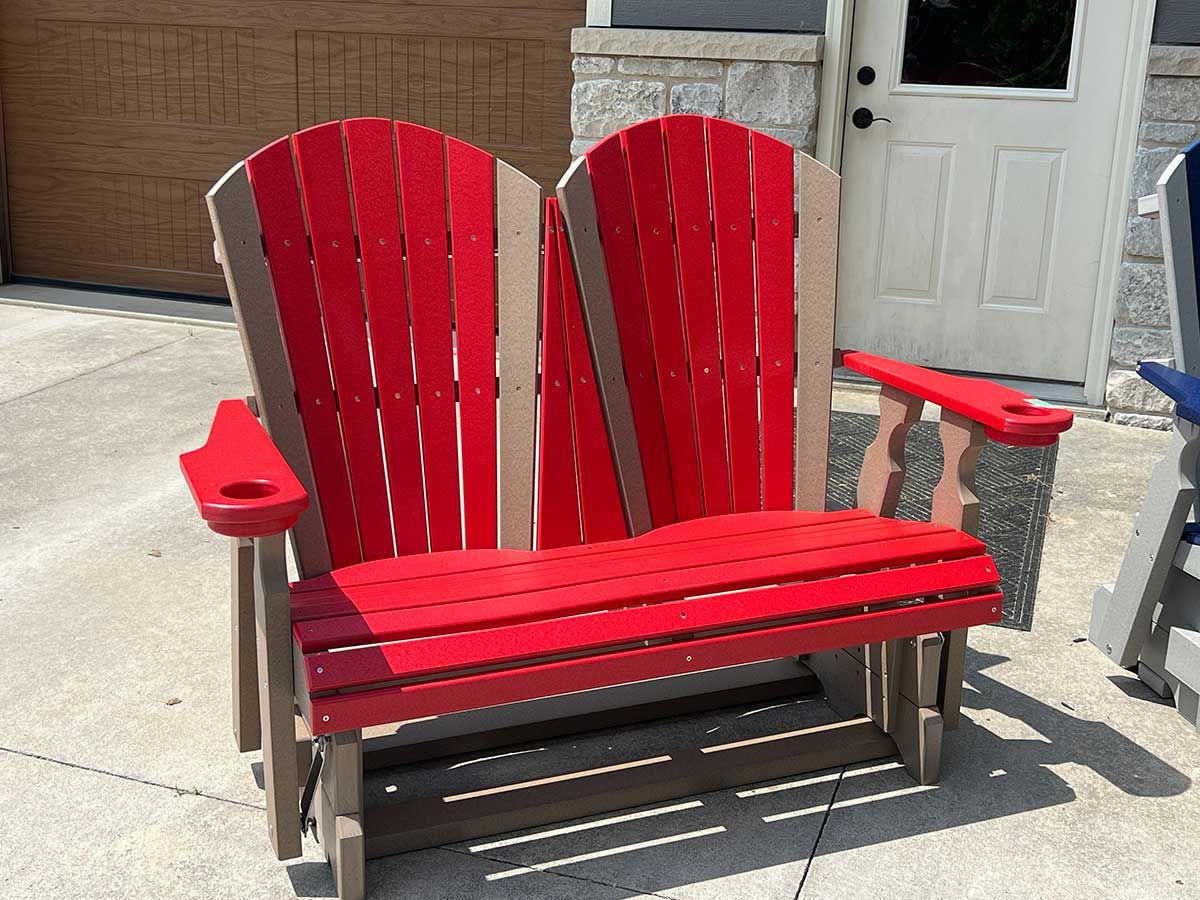A red and brown wooden bench is sitting on a sidewalk in front of a garage door.