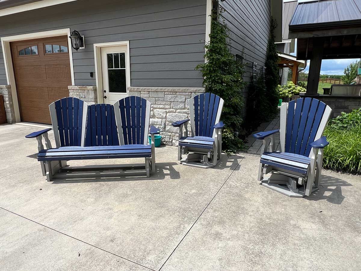 A set of blue and white adirondack chairs are sitting on a concrete patio in front of a house.