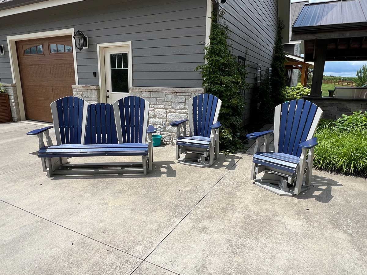 A set of blue and white adirondack chairs are sitting on a concrete patio in front of a house.