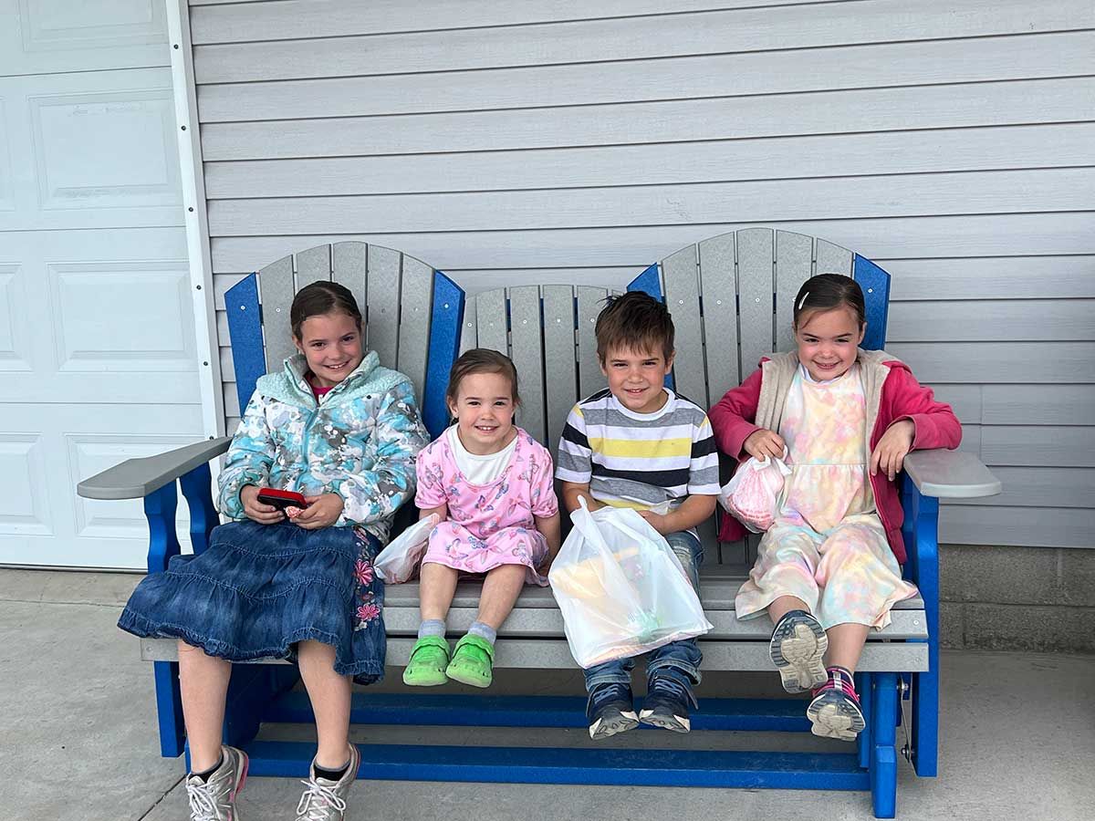 A group of children are sitting on a blue bench.