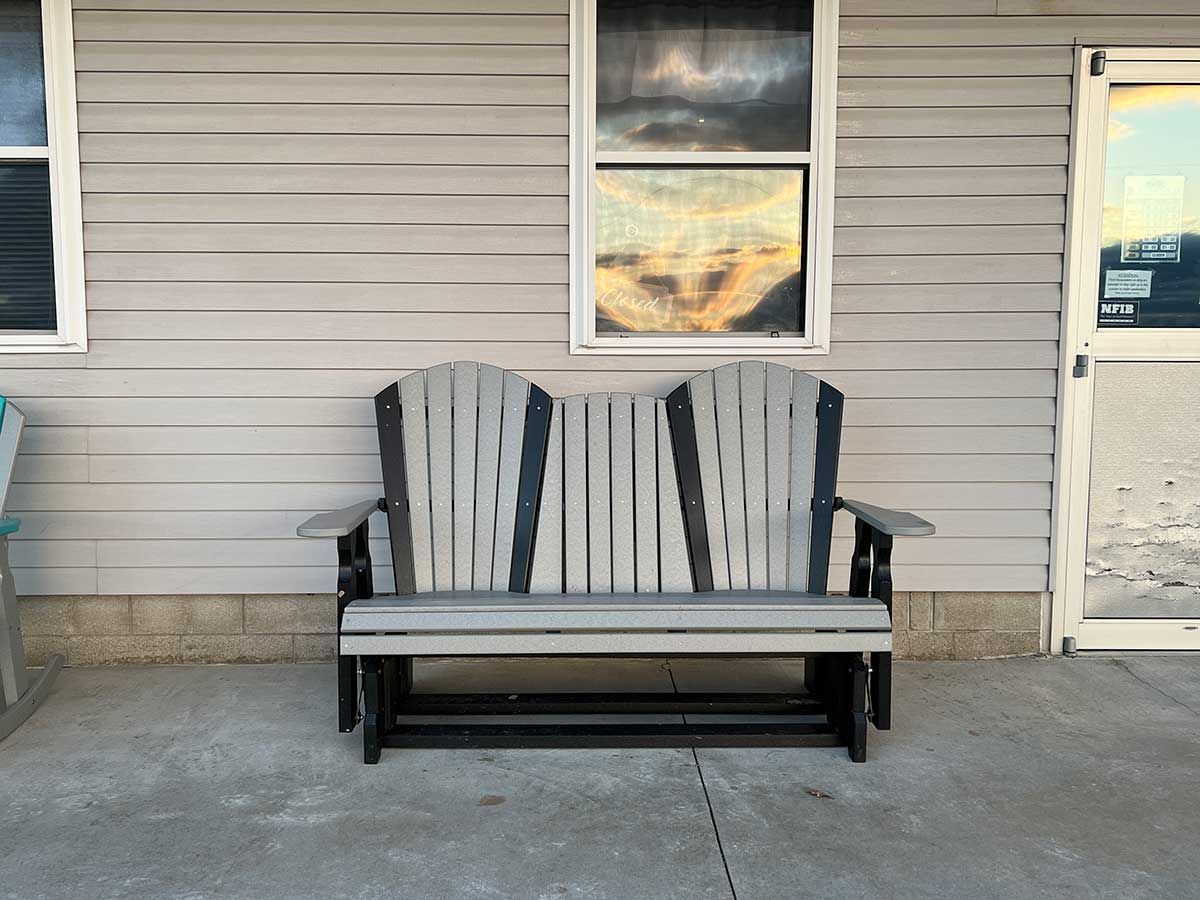 A bench is sitting in front of a house with a window.