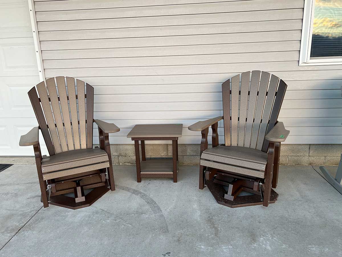 Two rocking chairs and a table are on a patio in front of a house.