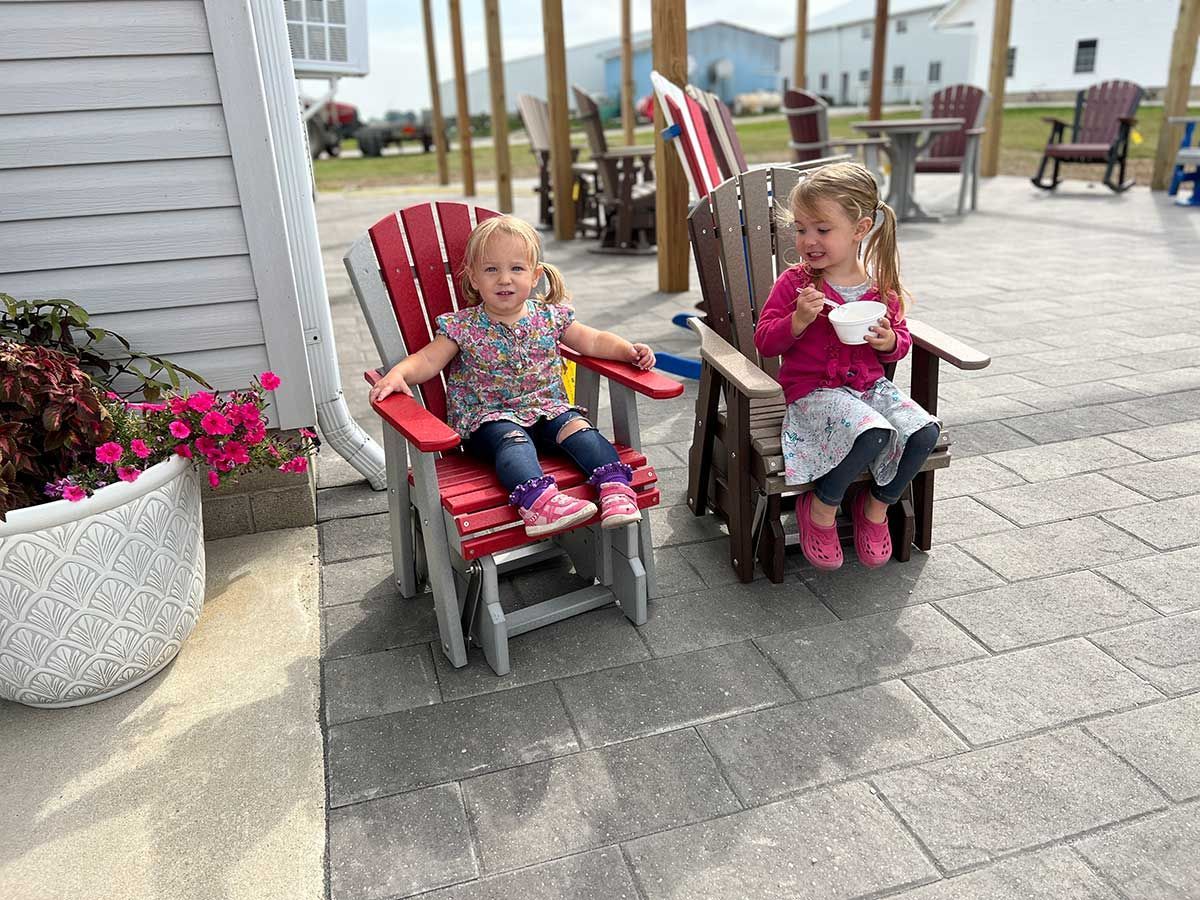 Two little girls are sitting in chairs on a patio eating ice cream.