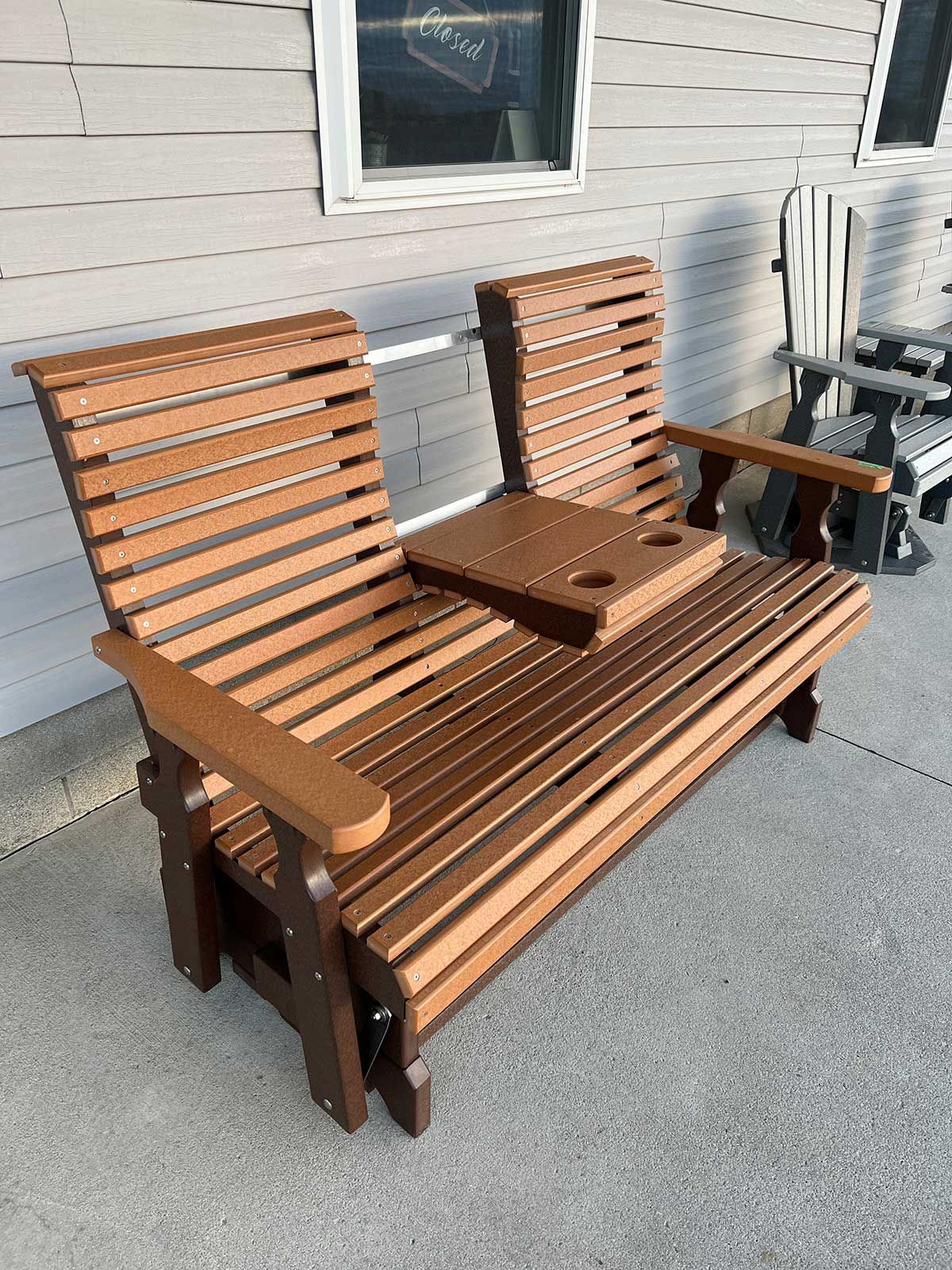 A wooden bench with a tray on it is sitting on a sidewalk in front of a house.