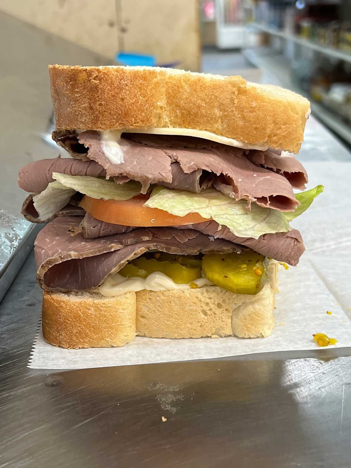 A sandwich with roast beef , lettuce , tomatoes and pickles is sitting on a table.