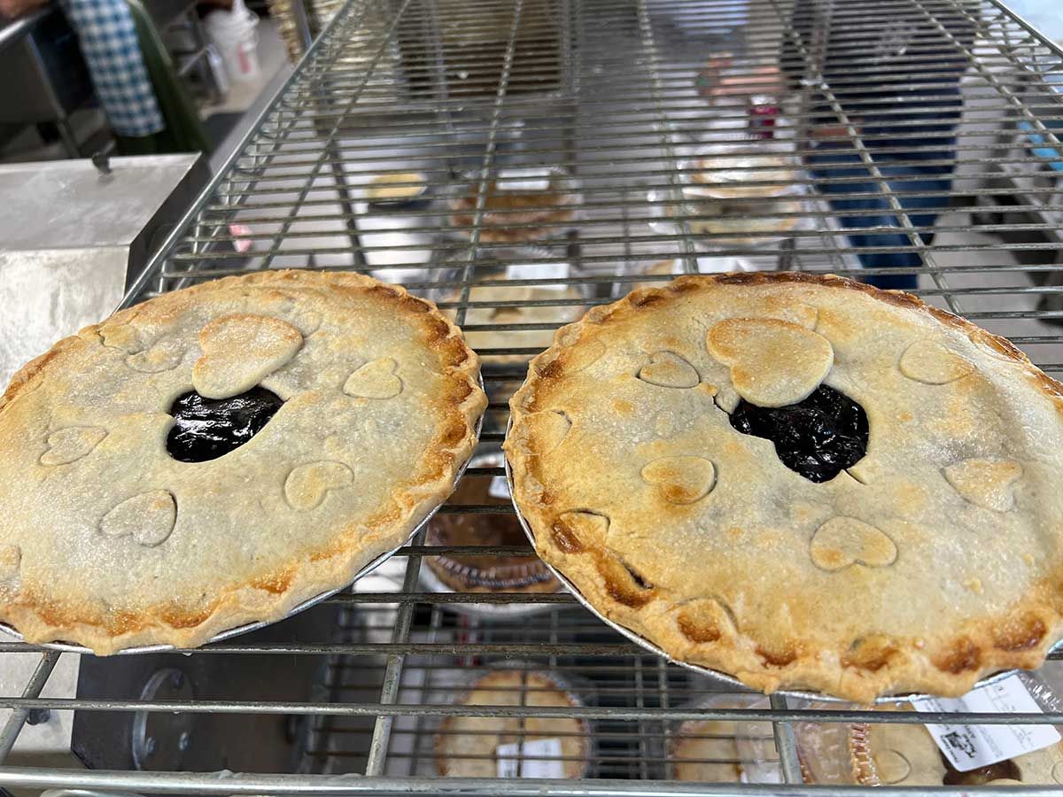 Two pies are sitting on a wire rack in a bakery.