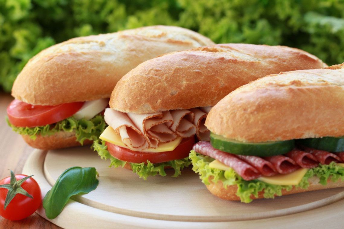 Three sub sandwiches are sitting on a wooden cutting board.