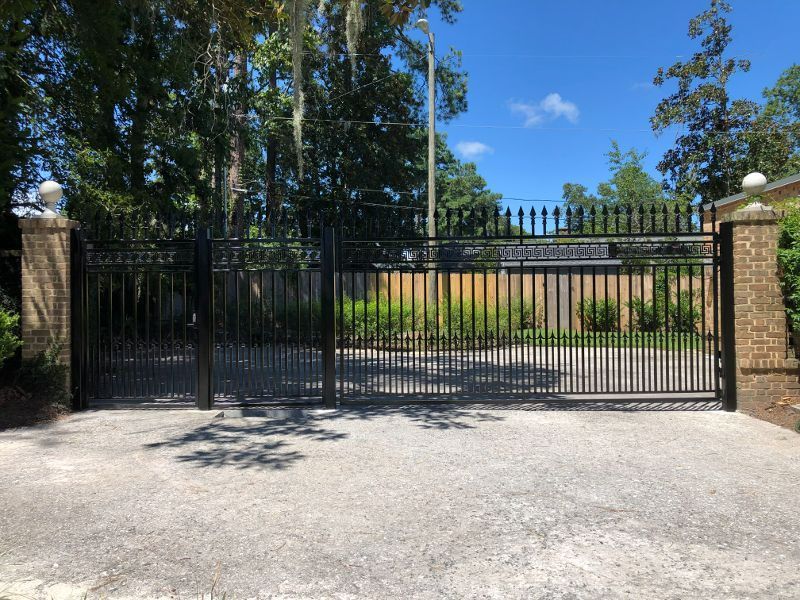 A black metal gate is closed on a gravel driveway.
