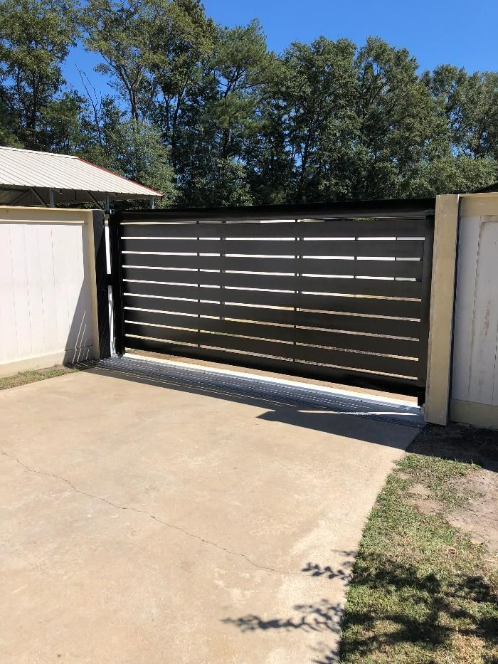 A sliding gate is open in a driveway next to a garage.