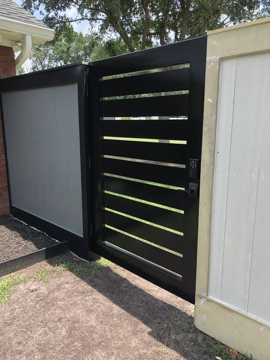 A black gate is sitting next to a brick wall.