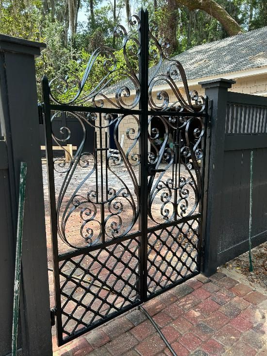 A wrought iron gate is sitting on a brick sidewalk next to a fence.