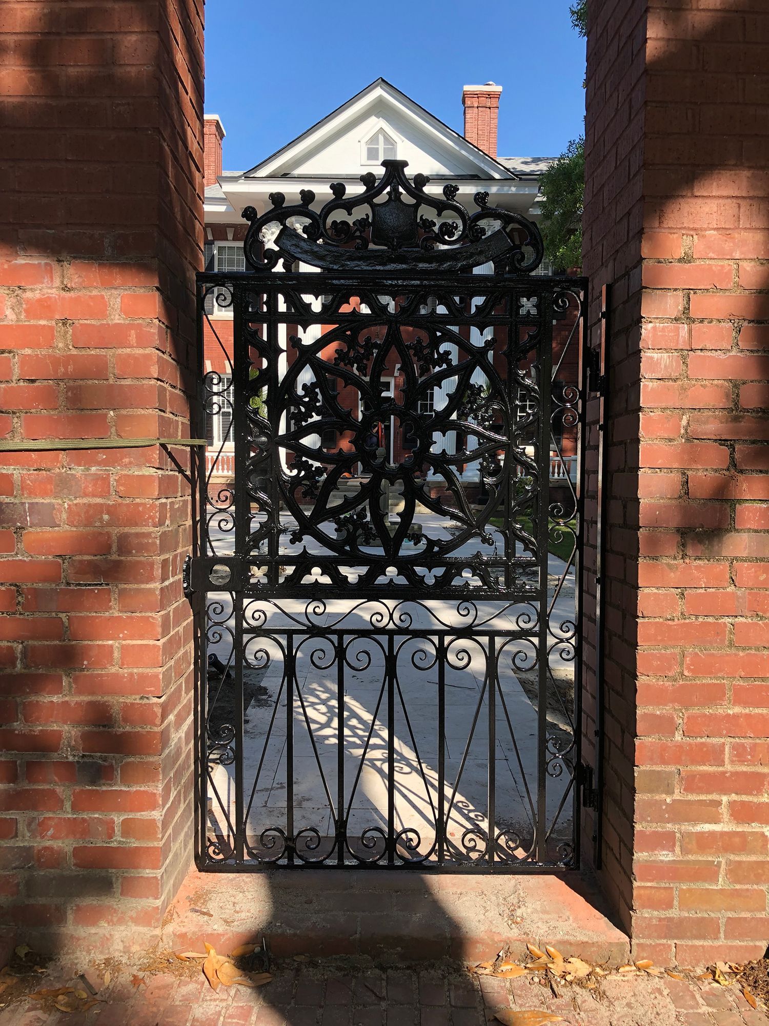 A wrought iron gate between two brick walls with a house in the background.
