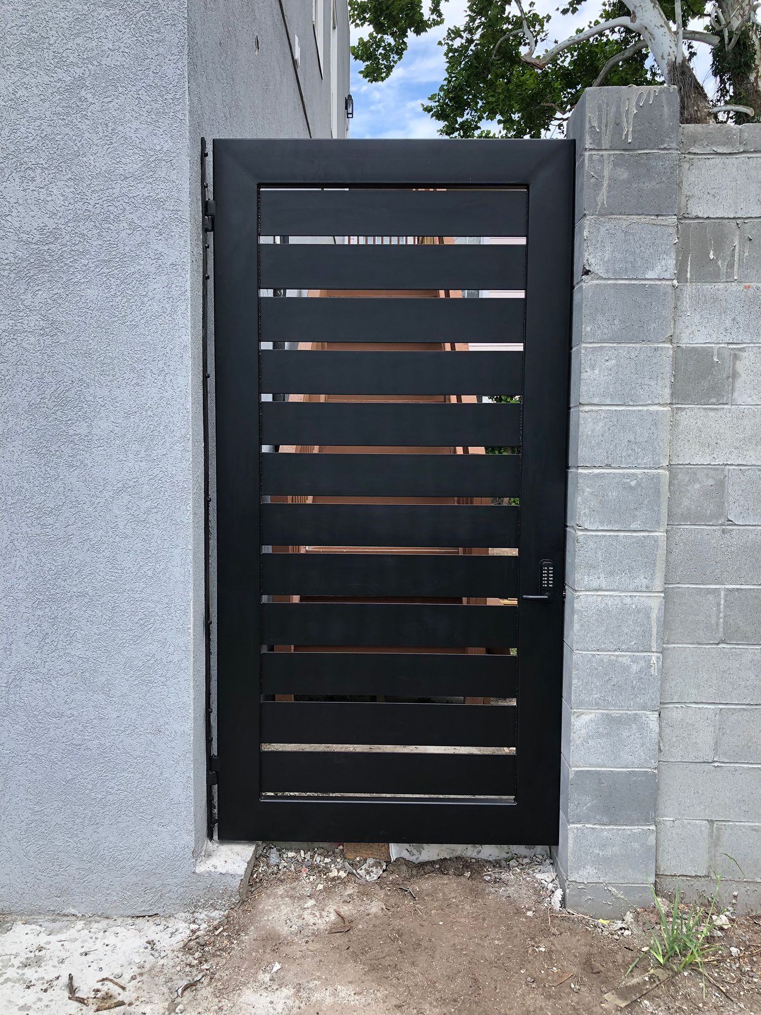 A black gate is sitting next to a brick wall.