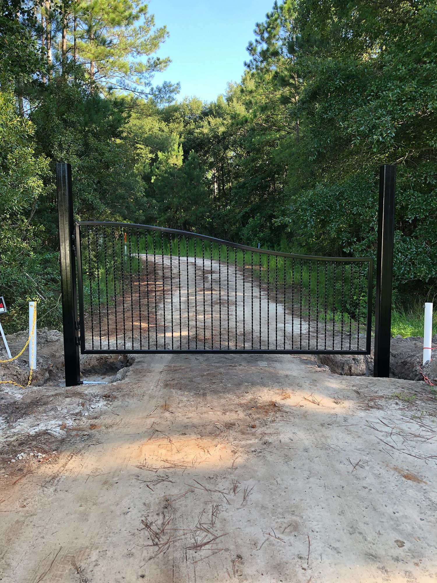 A black gate is sitting on the side of a dirt road.