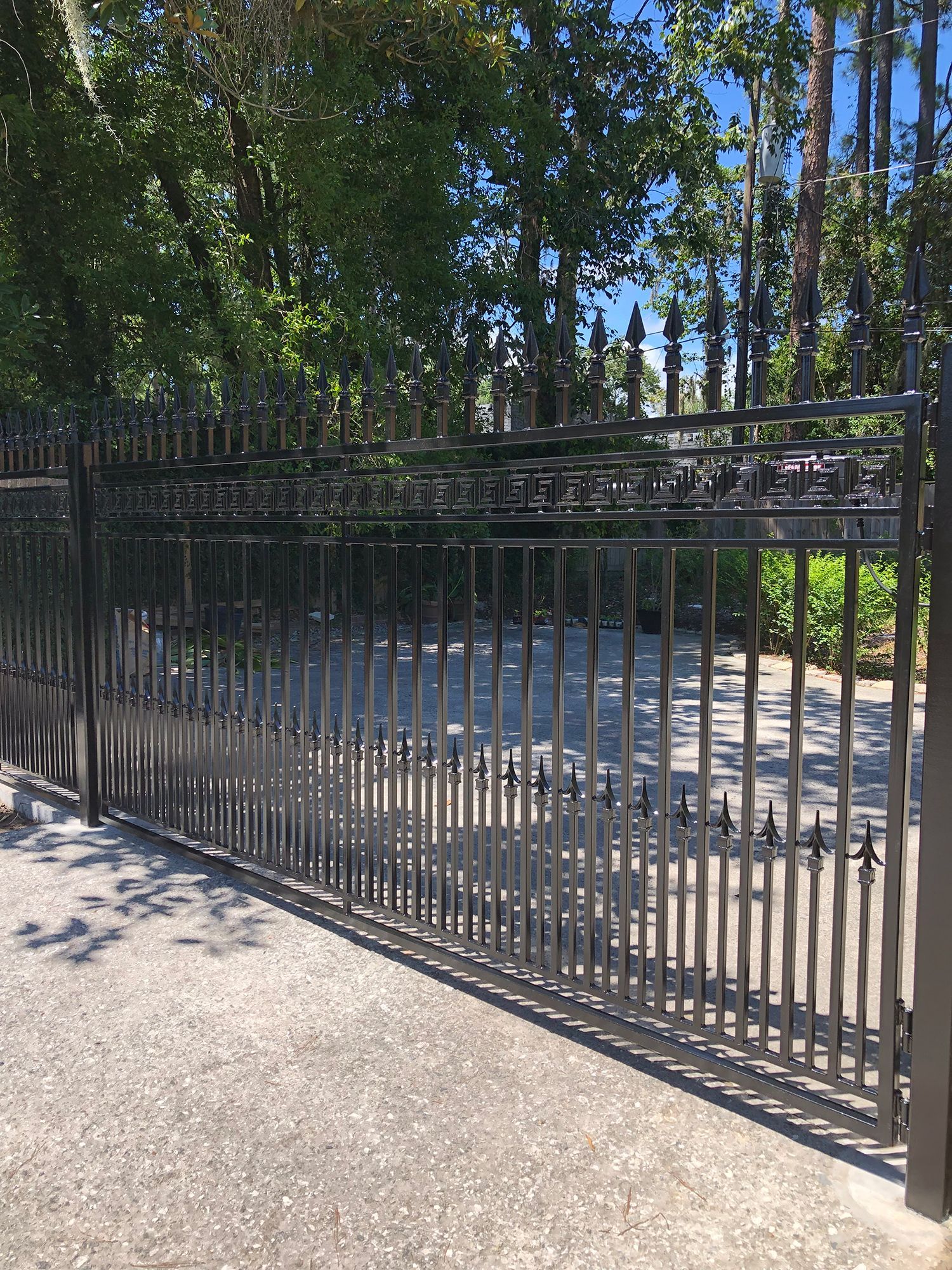 A black wrought iron gate is surrounded by trees on a sunny day.