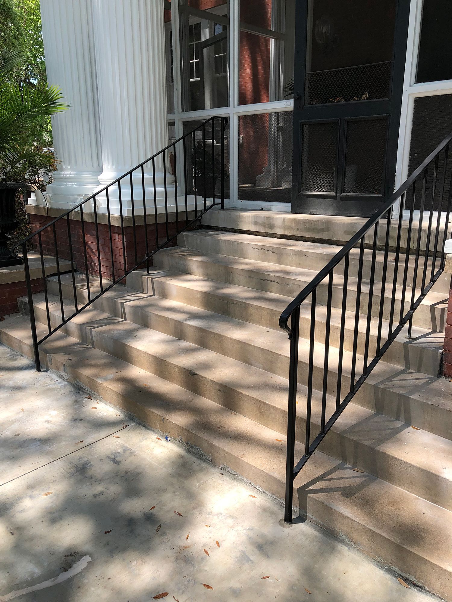 A wrought iron railing on a set of stairs leading up to a screened in porch.