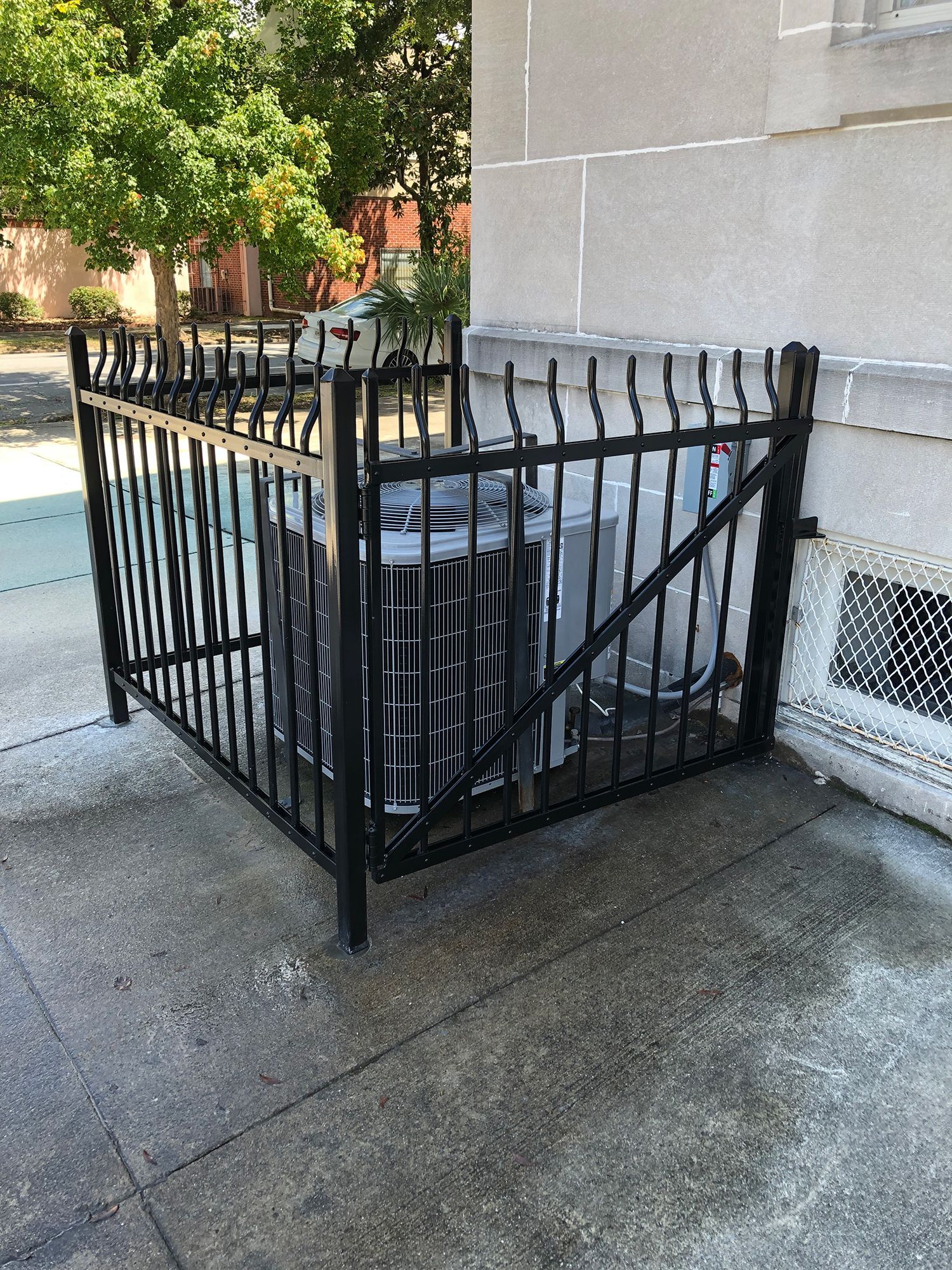 A black wrought iron fence surrounds an air conditioner on the side of a building.