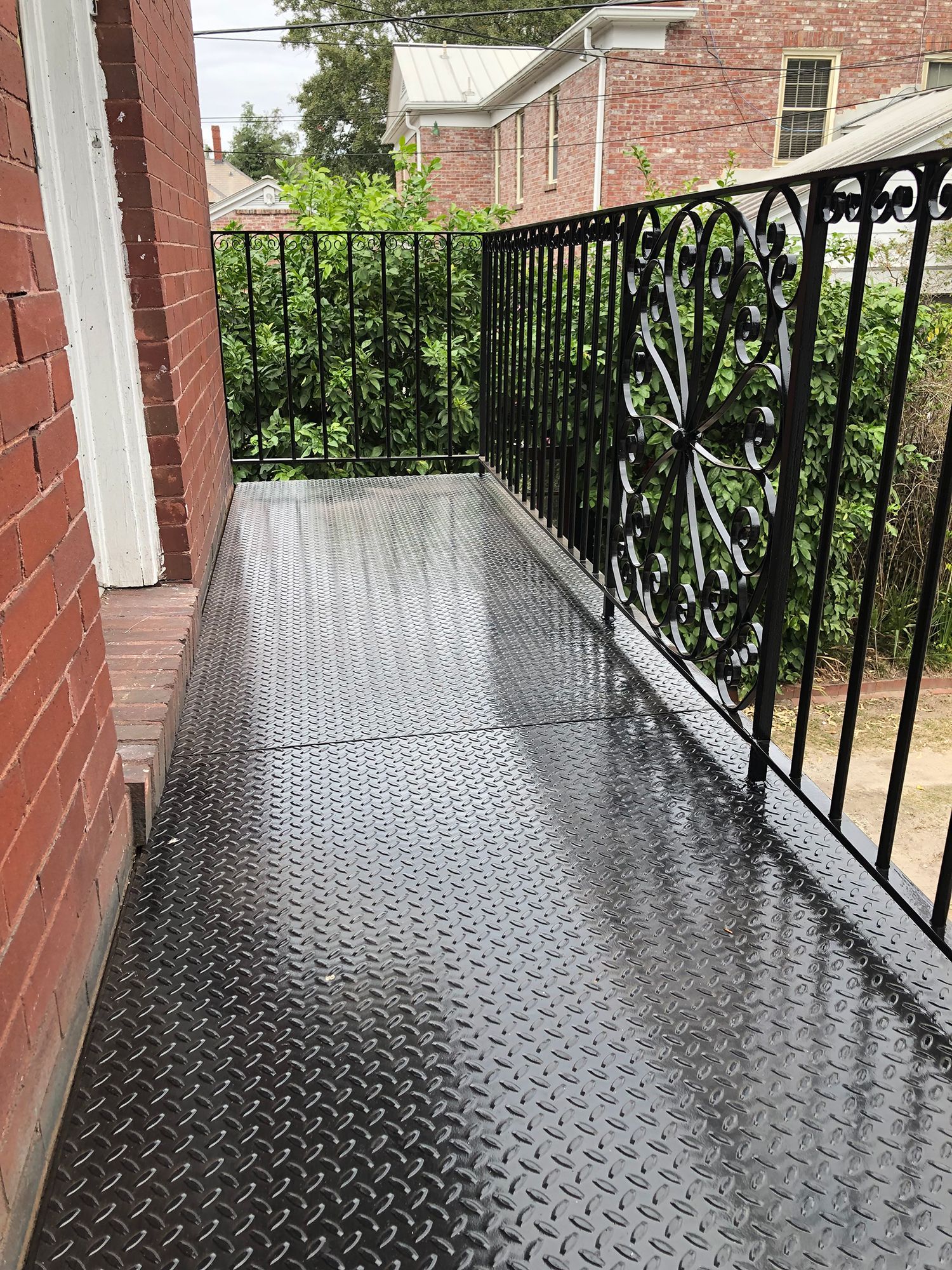 A balcony with a wrought iron railing and a brick building in the background.