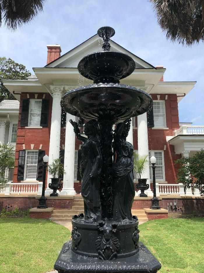 A fountain in front of a large brick house